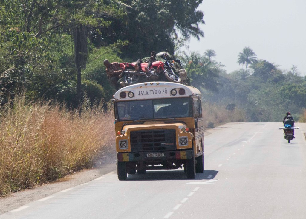 Overloaded old school bus with motorbike and man on roof!
